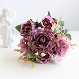 Detail shot of artificial purple roses with green leaves on a white vintage tabletop