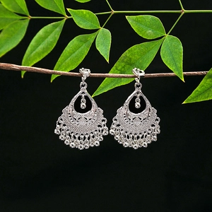 Detailed view of silver ethnic earrings with hollow patterns and tassel bells on a branch