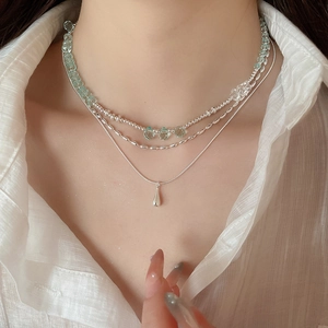 Detail of triple-layer necklace with green beads and silver waterdrop pendant on model