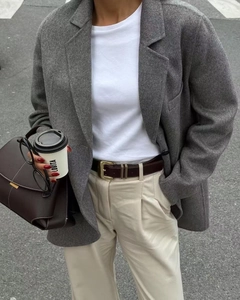 Detail of a dark brown leather belt with gold buckle on a grey wool blazer and beige pants