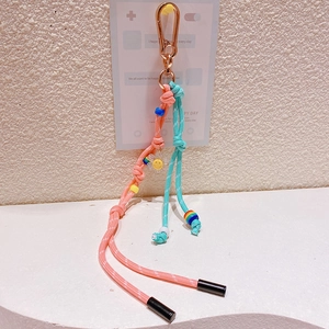 Détail du porte-clés tressé rose et turquoise avec fermoir doré et breloque fleur