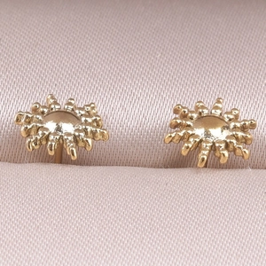 Macro shot of gold-plated sunburst stud earrings on a pink velvet jewelry display