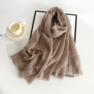 Close-up of brown cotton linen scarf with frayed edges on a minimalist white table