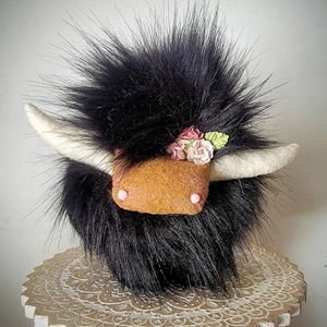 Detail of handmade black highland cow plush toy with floral decor on wooden stand