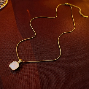 Detail of a gold titanium heart and moon necklace with a square pendant on a brown background