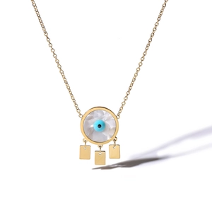 Macro detail of gold devil eye pendant with white shell inlay and metal tassels