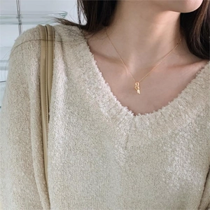 Close-up of a minimalist gold knot pendant necklace worn on a model with a beige sweater