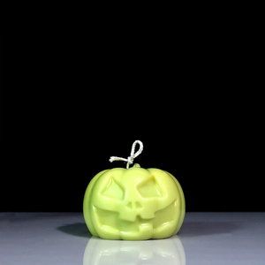 Detail of lime green pumpkin candle with carved facial features and cotton wick