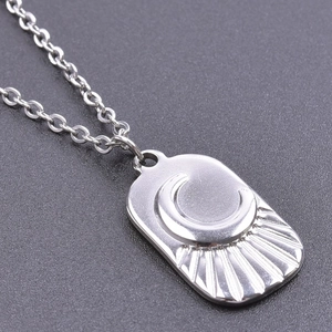 Detailed close-up of a silver stainless steel moon and sun relief pendant on a link chain