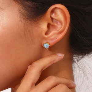 Close-up of a heart-shaped opal earring in gold setting worn by a female model