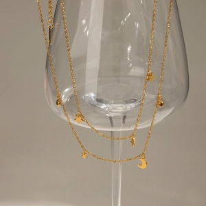 Layered gold stainless steel necklace with star and moon pendants on a glass