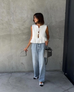 Detail of white sleeveless pleated top with tie-up front and high-waisted denim jeans