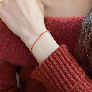Close-up of a handmade red woven bracelet with gold beads worn on a woman wrist