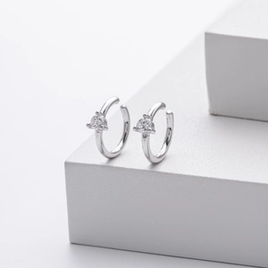 Macro shot of silver C-shaped ear cuff with sparkling heart-shaped zircon on white blocks