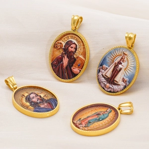 Macro detail of 18k gold-plated oval religious pendants with St. Benedict and Jesus icons