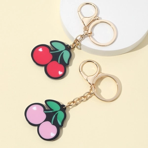 Cute cherry keychain pendants in red and pink resin with gold metal chain on beige surface