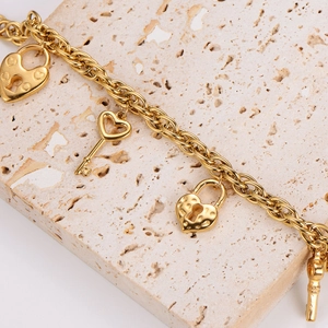 Gros plan sur le bracelet en acier doré avec breloques cadenas cœur et clé