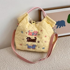 Detail of yellow quilted tote bag featuring cute cartoon cat embroidery and pink straps