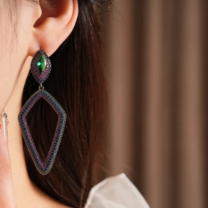 Close-up of vintage geometric floral earrings with green stone and colorful zircons