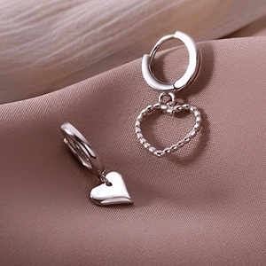 Macro detail of asymmetric silver heart earrings on smooth purple silk fabric