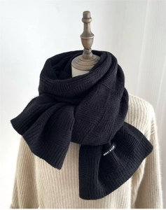 Detailed close-up of black checkered knit scarf showing texture and brand label