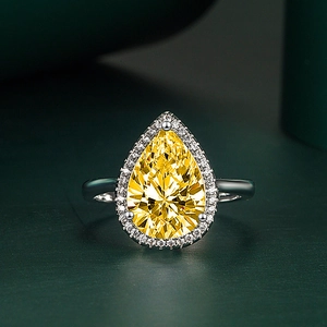 Macro shot of a pear-shaped yellow zircon ring with a halo of white stones on a silver band