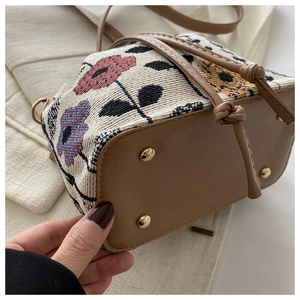Detail view of ethnic floral tapestry bucket bag with brown leather base and metal feet