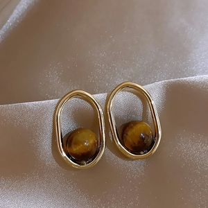 Detail of tiger eye stone earrings with golden oval frames on beige satin fabric