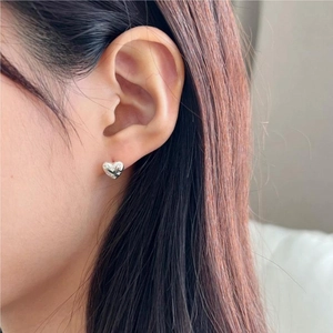 Close-up of silver heart-shaped stud earrings with quilted texture on female model's ear