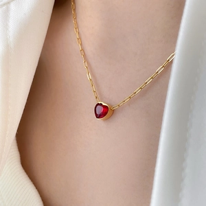 Close-up of a red heart-shaped gemstone pendant on a gold paperclip chain necklace