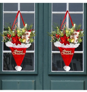 Detail of red plush Santa hat door hanger with pine needles, red flowers and LED lights