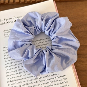 Detail showing a light blue fabric scrunchie resting on an open book over a wooden desk