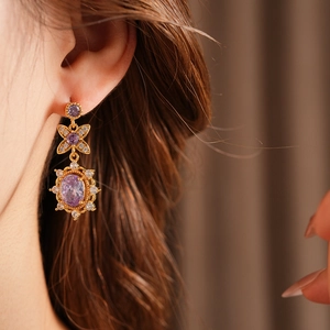 Detailed view of vintage gold drop earrings with purple gemstones and zircons on model