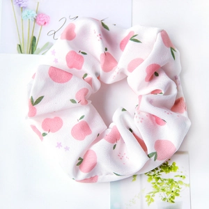 Detail of white fabric scrunchie with pink peach patterns and green leaves