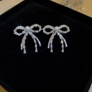 Sparkling silver bow earrings with artificial pearls and tassels on black velvet background
