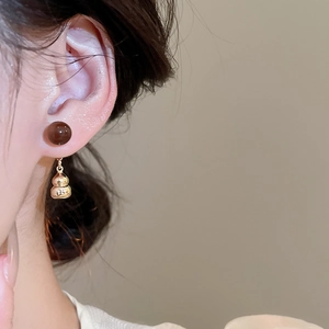 Close-up of vintage gourd drop earrings with brown beads worn by a model