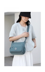 Detail of grey-blue waterproof nylon crossbody bag with multiple zipper pockets and logo
