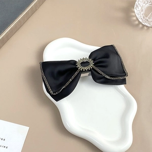 Detailed view of a black satin bow hair clip with sparkling rhinestone edges and metal clip