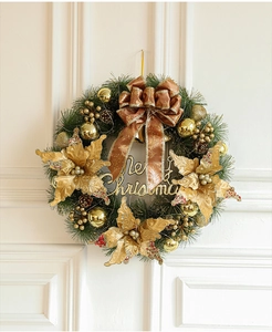 Detail of a Christmas wreath with gold ornaments and Merry Christmas sign on a white door