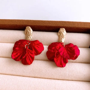 Detail view of red acrylic petal earrings with textured gold studs in a velvet box