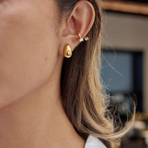 Detail of golden teardrop earring and heart-cut zircon ear cuff on model ear