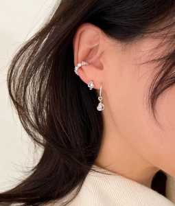 Macro view of silver heart ear cuffs and rhinestone stud earrings on model's ear