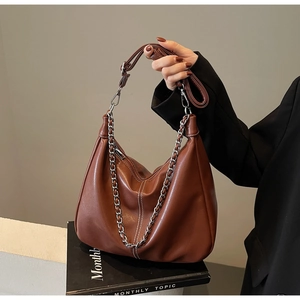 Detail of brown PU leather shoulder bag with white stitching and silver chain strap