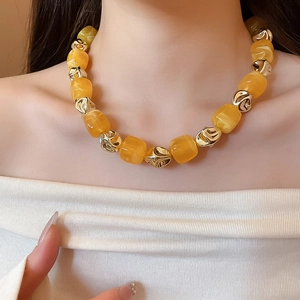 Detail of yellow acrylic beads and gold irregular metal accents on a necklace worn by a model