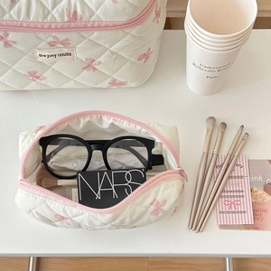 Macro view of cream quilted cosmetic bag featuring pink bow patterns and a zipper