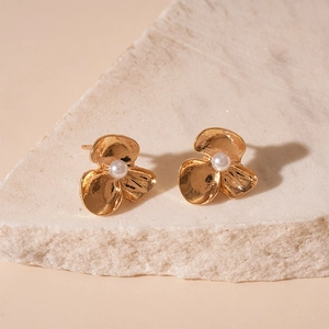 Macro detail of golden flower earrings featuring hammered metal texture and white pearl