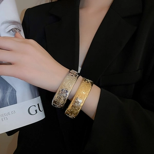 Close-up of gold and silver open bracelets with intricate floral embossed patterns