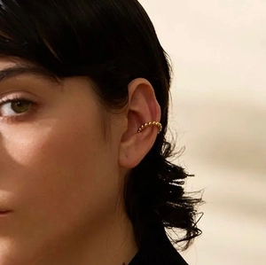 Close-up of golden beaded ear cuff clip-on earring worn on a model's ear cartilage