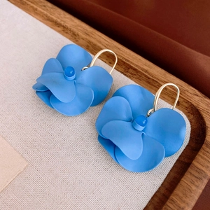 Close-up of matte sky blue flower drop earrings with golden metal hooks on a soft tray