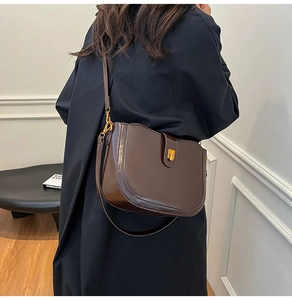 Detail of vintage brown saddle bag with gold buckle on a model wearing a black coat